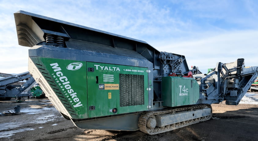 A green and black machine positioned on a dirt surface, indicating its use in construction or landscaping activities.