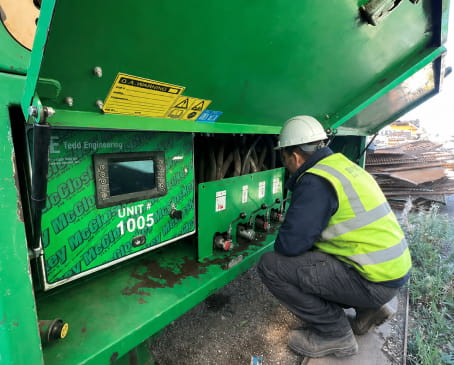 A man wearing a safety vest operates a machine, focusing on his task in a work environment.