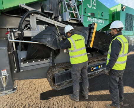 Two men in yellow vests operate a large machine, focused on their tasks in an industrial setting.