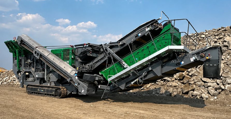 A large green-and-grey McCloskey rock crusher with conveyor belts and tank tracks on a sunny, rocky job site.