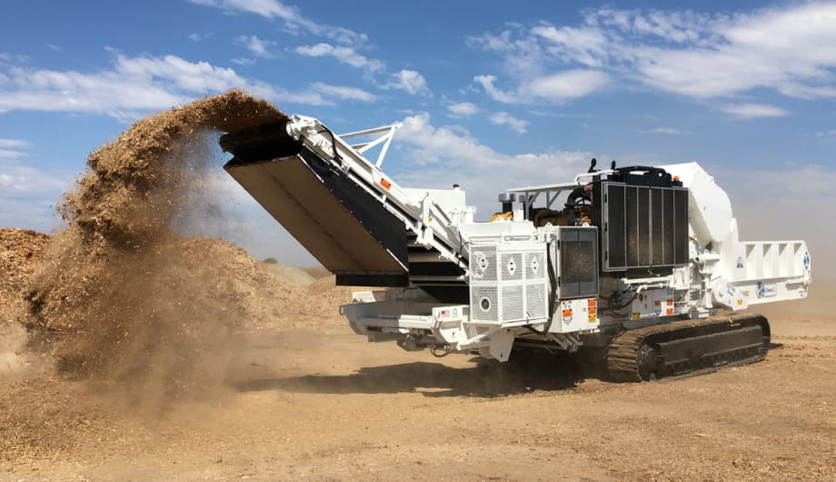 A large machine is actively dumping sand, creating a sizable pile on the ground.