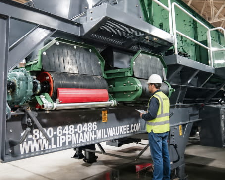 A man stands beside a large industrial machine, showcasing its size and complexity in a work environment.