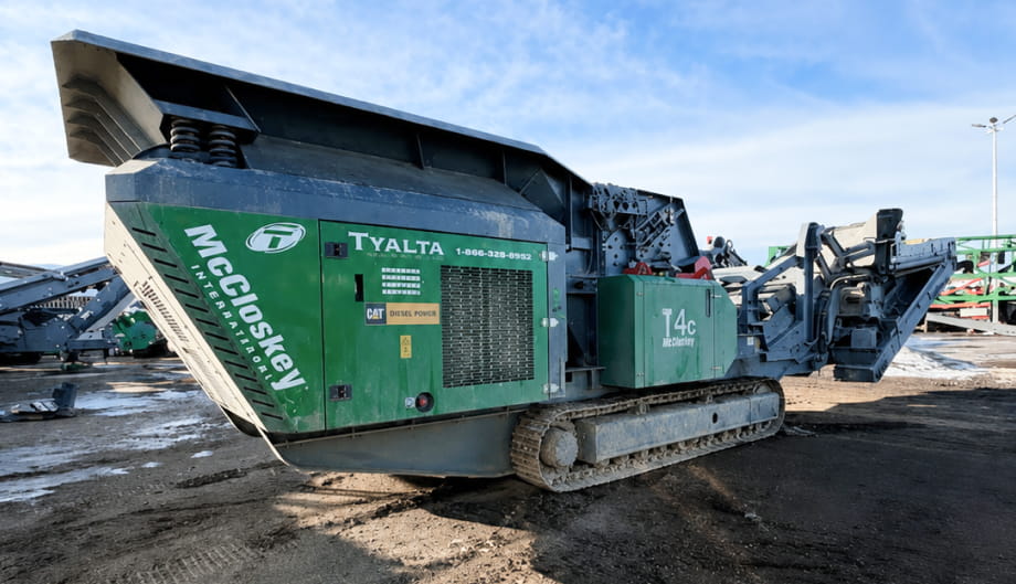 A green and black machine positioned on a dirt lot, surrounded by bare ground and construction debris.